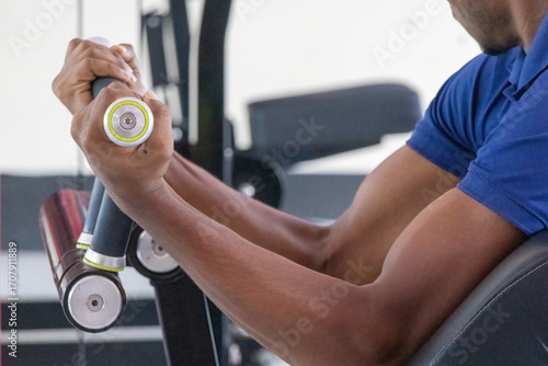 Obraz na plátně Close-up of a man's hand gripping a handle and lifting a plate-loaded bicep curl machine, showcasing focused muscle building and strength training in a modern gym