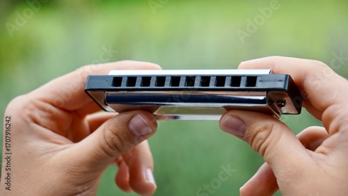  kid's hands holding a harmonica against natural background    