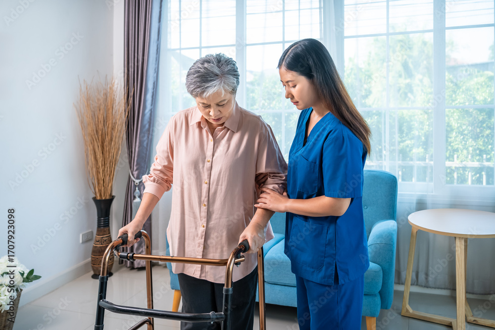 Fototapeta premium Elderly Asian woman walking with nurse assistance and walker at home