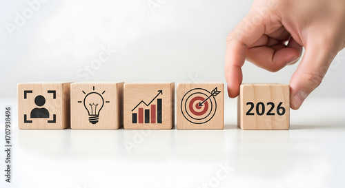 Hand placing wooden block with 2026 year on a row of business concept blocks.