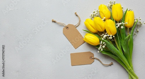 Bright yellow tulips paired with delicate white baby's breath, alongside blank rustic tags on a serene gray backdrop create a gentle scene.
