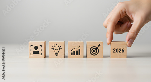 Hand placing wooden block with 2026 year on table with business icons.