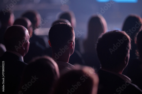 Rear view audience during Gdynia conference, spotlight head rim lighting, landscape telephoto bokeh, engaged mood, useful for corporate keynote brochure