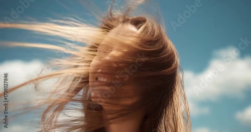 Feeling breeze, woman tilting head back, whipping hair, revealing radiant smile under blue sky