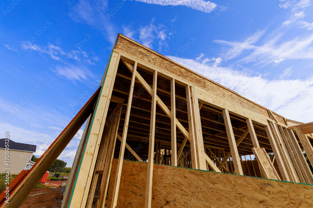 Fototapeta premium Workers are building house wooden frames beams in residential neighborhood, wooden structures, clear weather.