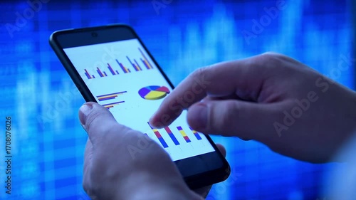 Businessman hands using a smart phone displaying financial data, against a vibrant blue stock market background. Concept of trading.