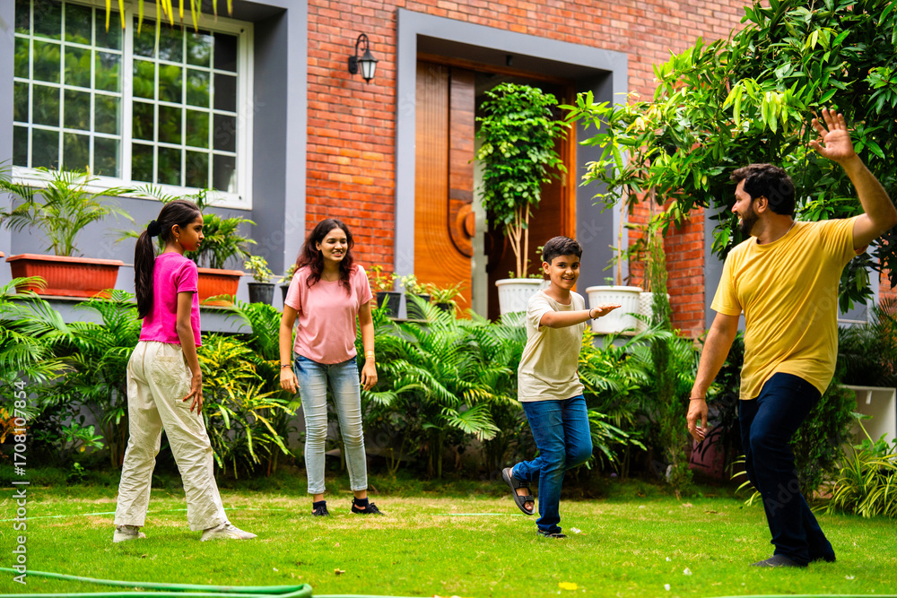 Fototapeta premium Indian family playing Langdi or one-leg hop game in garden, enjoying energetic outdoor fun