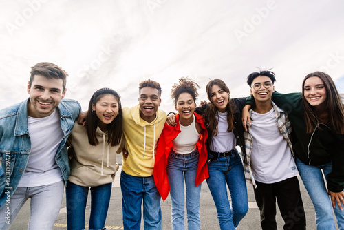 Young group of teenage friends smiling at camera hugging each other outdoors. Unity, friendship lifestyle and youth community concept