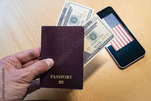 Hand holding passport with US dollars and smartphone displaying american flag, suggesting ESTA application and fee increase