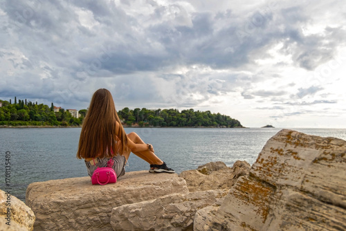 Canvas Print Girl sitting on seaside rocks under cloudy sky