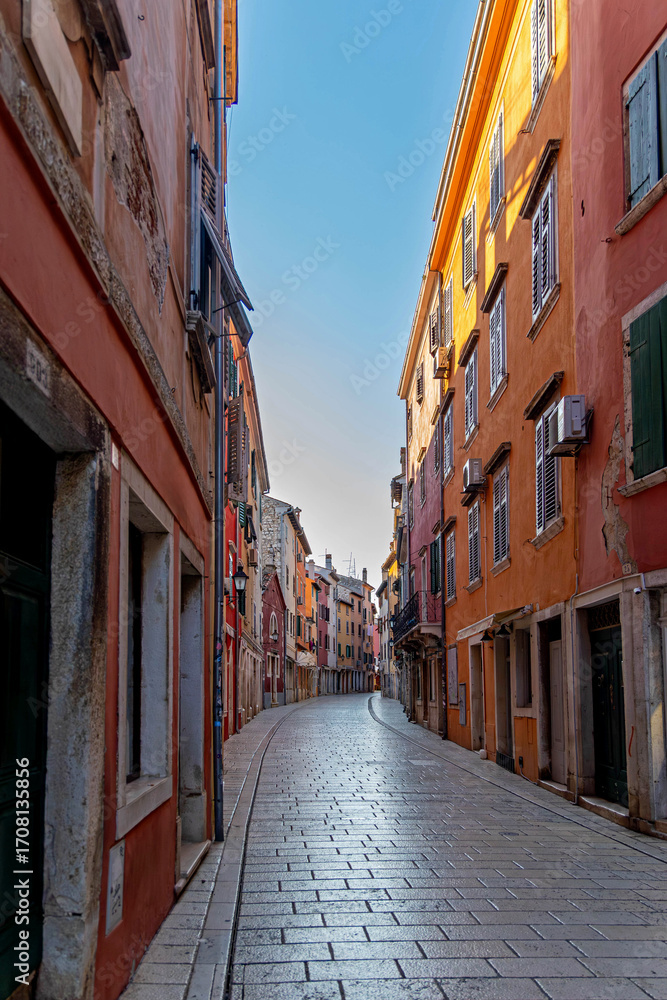 Fototapeta premium Empty colorful street in historic European town. Charming narrow street lined with colorful, aged buildings in a historic European town, captured in early morning light and silence.