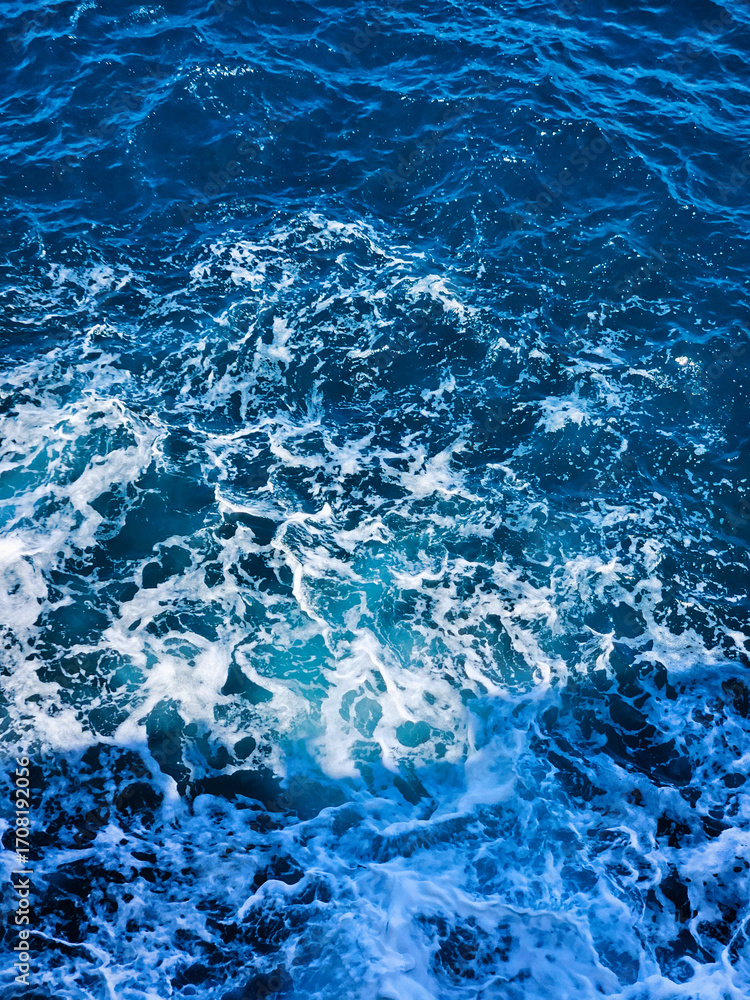 Fototapeta premium Water wave background. Turbulent ocean waves from above in blue tones. Aerial view. White wave splashing in the deep sea. Top view background photo of ocean sea water. Ocean surface. Navy blue.