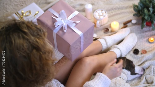 Relaxed woman in white sweater sitting on blanket with sleeping dog, surrounded by warm christmas decorations and softly glowing candles