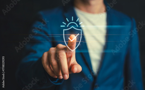 Businessman touching a virtual glowing shield icon with a checkmark and sunburst, symbolizing data security, protection, and verified digital wellness.