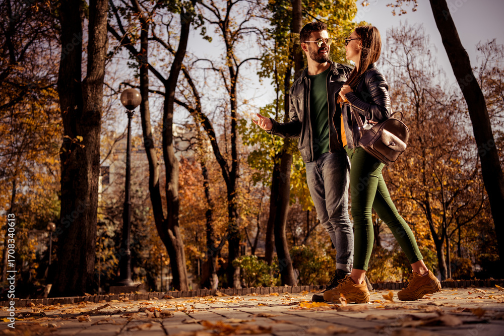 Fototapeta premium Young couple enjoying a romantic walk in an urban park surrounded by beautiful autumn foliage during sunny weather