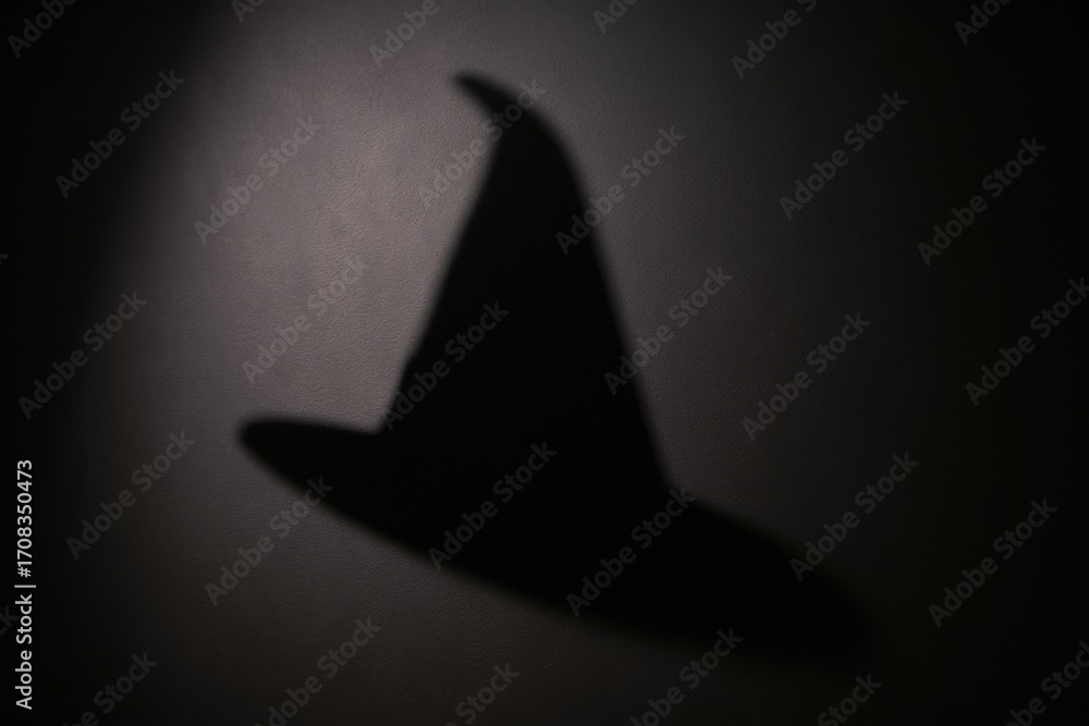 Fototapeta premium A shadow of a witch's hat cast on a dark background, evoking a mysterious and magical atmosphere.