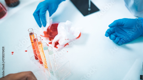 A laboratory accident shows red liquid spilled near test tubes as gloved hands attempt cleanup, symbolizing contamination risks, safety awareness, and the importance of strict lab protocols.