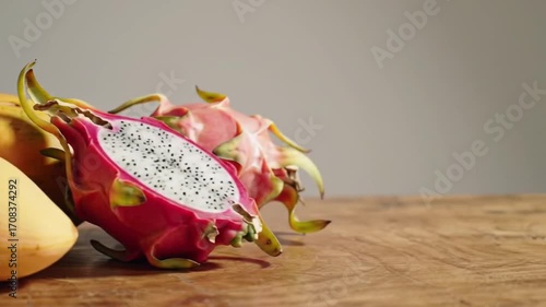 Exotic tropical fruits, featuring a vibrant sliced pitaya or dragon fruit and a ripe mango, arranged on a rustic wooden table with copy space