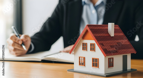 Real estate agent reviewing property documents with a model house on the table for home buying or selling consultation in a professional setting