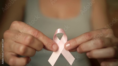 Close-up of female hand holding pink satin ribbon, symbolizing support for breast cancer awareness, medical care, and self-examination.