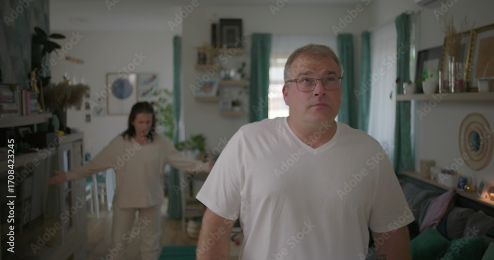 Obraz premium Man standing visibly upset during argument with woman in background, relationship tension in living room, emotional and dramatic moment of disagreement