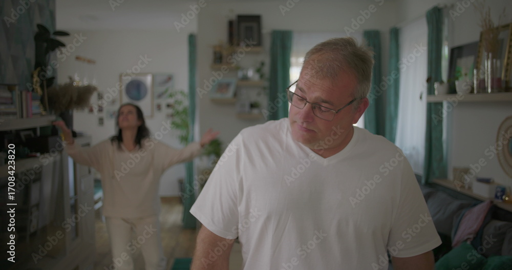 Obraz premium Man standing visibly upset during argument with woman in background, relationship tension in living room, emotional and dramatic moment of disagreement