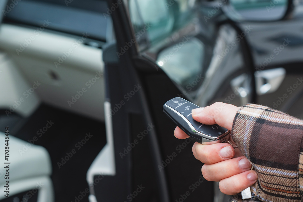 Obraz premium Close-up of a person holding a car key with a remote control in front of an open vehicle door. Concept automotive access, smart keys, car security and modern transportation.