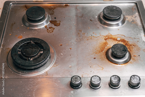 Dirty stove with food leftovers. Unclean gas kitchen cooktop with greasy spots, old fat stains, fry spots and oil splatters.