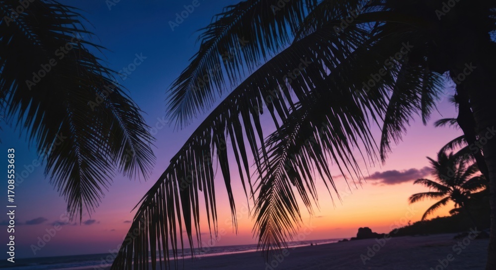 Fototapeta premium Silhouetted palm trees frame a vibrant sunset over a tranquil beach