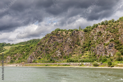 Schieferfelsen am Rhein mit Weinbergen im Oberen Mittelrheintal bei St. Goarshausen in Rheinlandpfalz, Deutschland mit dunklen Wolken. NSG Rheinhänge von Burg Gutenfels bis zur Loreley