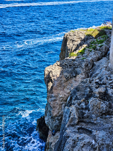 The rock face shows layers of erosion. The waves of the blue ocean are raging, beating against the coastal cliffs. Cabo de mar con agua azul. Playa rocosa de agua turquesa. Sea and sky.