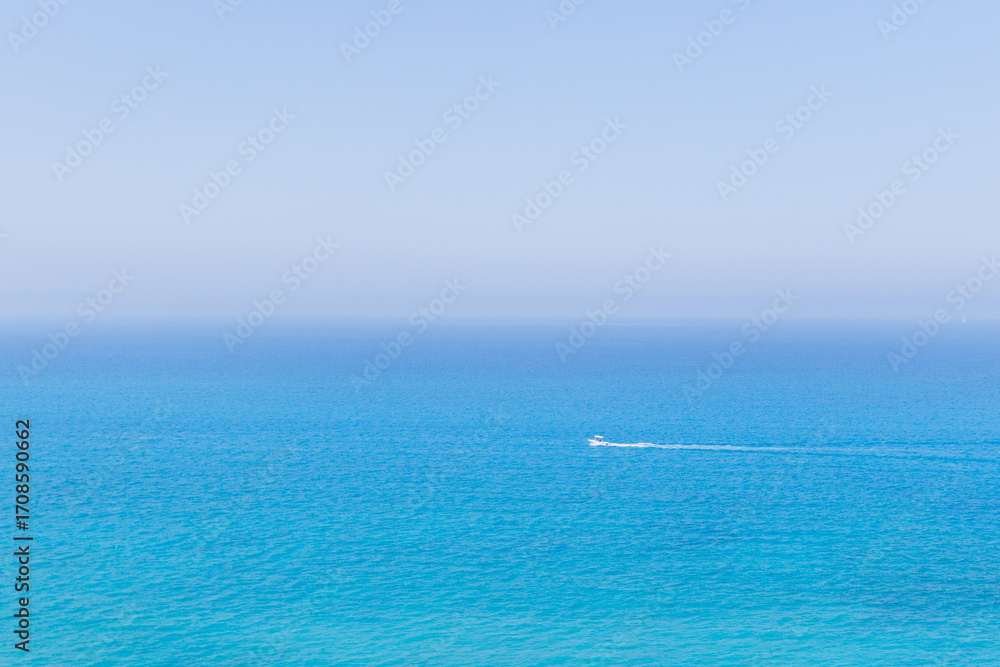 Obraz premium Serene expanse of blue ocean with a motorboat is wake in the foreground and a distant sailboat, perfect for travel, lifestyle, or maritime branding.