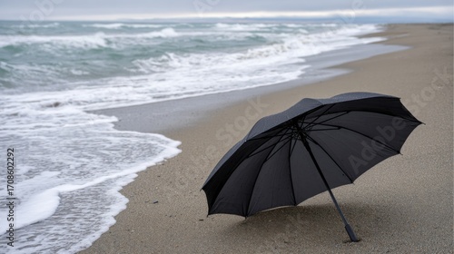 Open black umbrella lying abandoned on the beach, waves approaching, symbol of protection and surrender