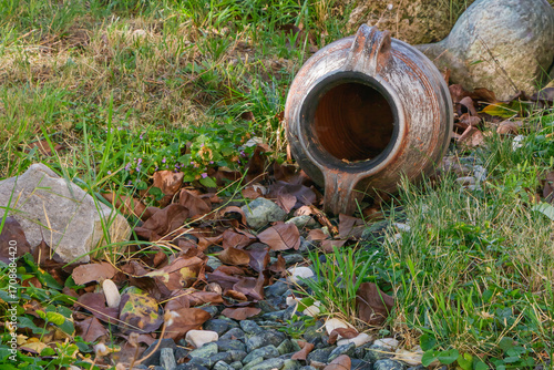 Wallpaper Mural Old clay amphora lying on ground with dry leaves, grass, and stones creating rustic outdoor garden scene Torontodigital.ca