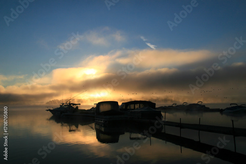 Early morning sunrise on the lake with boats and mist.