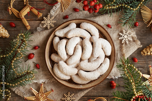 Homemade Christmas cookies called Kipferl or vanilla crescents coated in sugar on a plate with decorated spruce tree