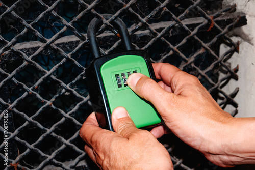 close-up of a man setting the code on a green lockbox on metal grate