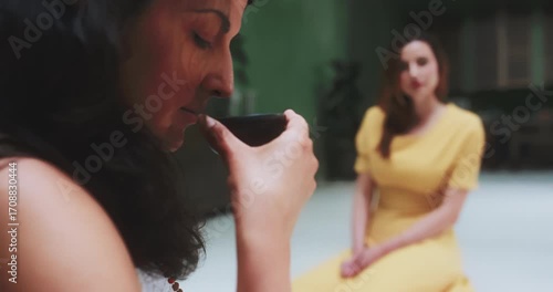Woman smelling tea as friend watches in background, close-up