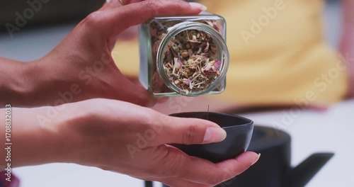 Elegant hands pouring loose tea leaves into bowl, close-up
