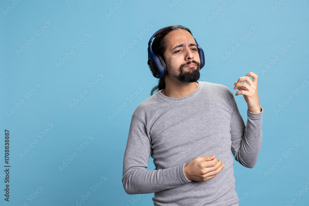 Fototapeta premium Relaxed person enjoying music on headphones expressing joy for leisure activity. Modern adult showcases enjoyment of audio entertainment and wireless gadgets in a professional studio.