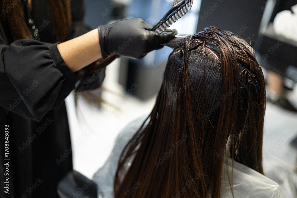 Naklejka premium A woman with long dark hair receiving a hair treatment at a salon, showcasing the expertise of her stylist.