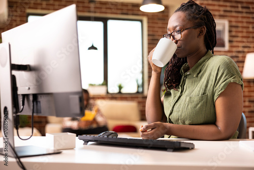 Photos Young female adult with glasses sipping coffee and reading online articles on computer