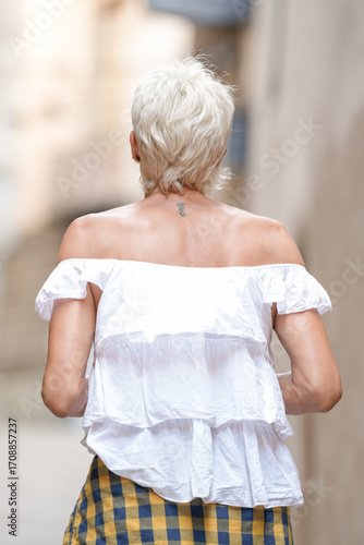 Photography A woman wearing a white shirt and yellow and blue plaid skirt walks down a street