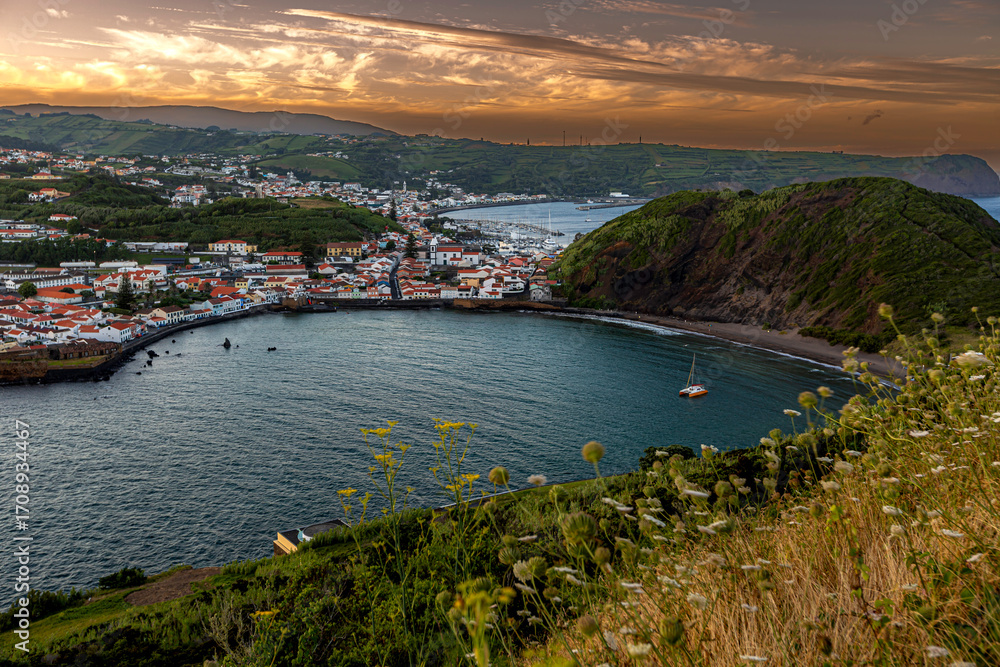 Fototapeta premium Faial, Azores, island, Portugal, Beautiful view of a bay with a boat in the water. The sky is orange and the water is calm