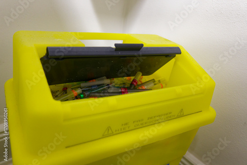 Yellow medical sharps container with lid and visible needles