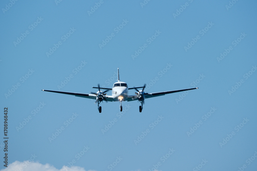 Fototapeta premium Small propeller plane flying in the blue sky on a sunny day. Twin-engine plane soaring through a clear blue sky.