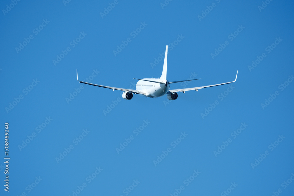 Obraz premium The plane that's just taken off drifts away from the airport across clear blue sky. Airplane flying in the blue sky on a sunny day. Airplane taking off, rear view. Travel concept.