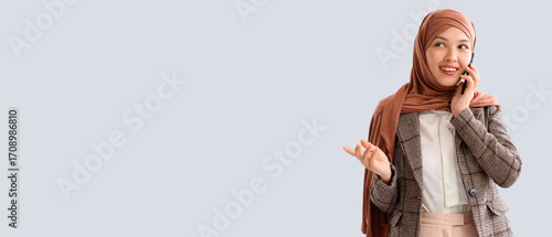 Young Muslim businesswoman talking by mobile phone on light background