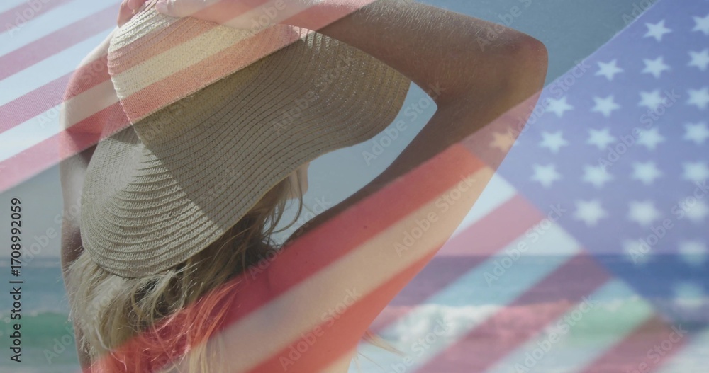 Fototapeta premium Gazing female beachgoer wearing straw sunhat and red bikini top at shoreline, with flag overlay