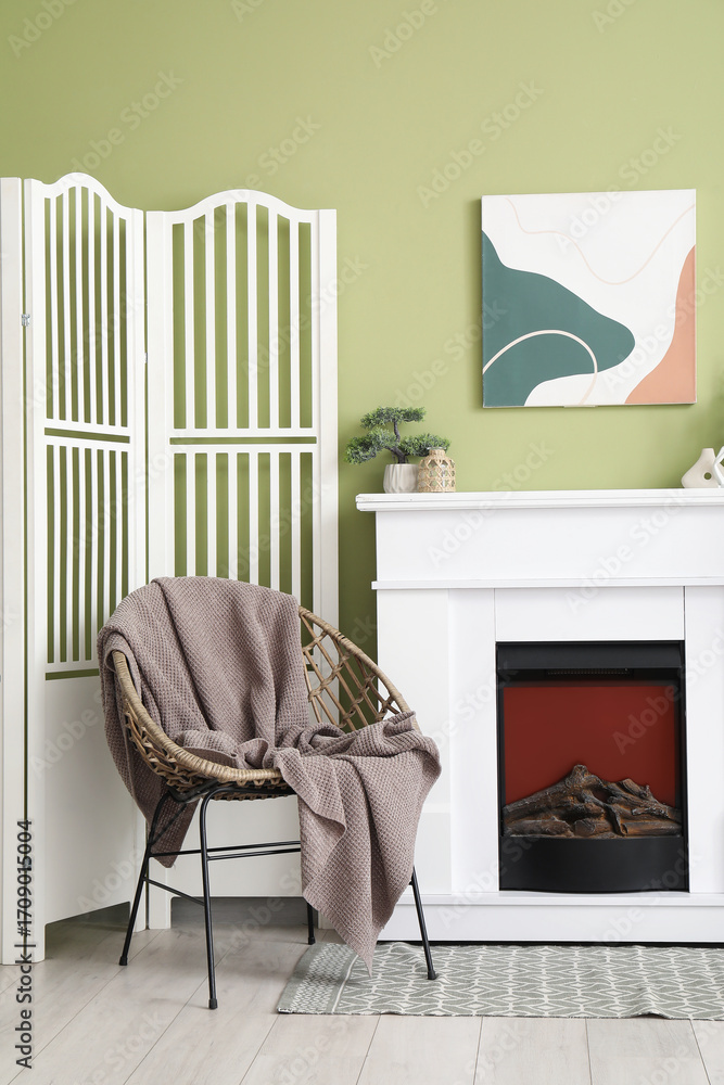 Fototapeta premium White fireplace, houseplants, armchair and folding screen in interior of stylish living room